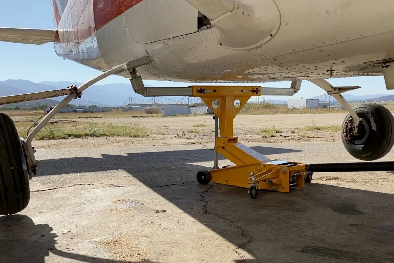 A yellow crane is attached to the wing of an airplane.