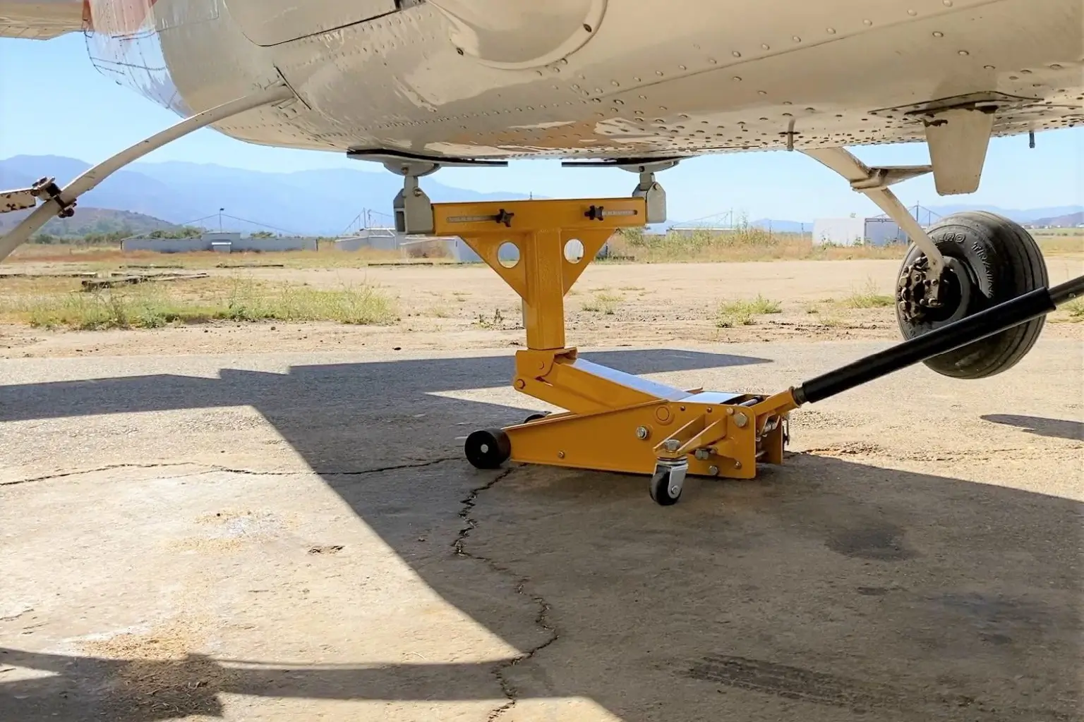 A yellow jack stands under an airplane on the ground.